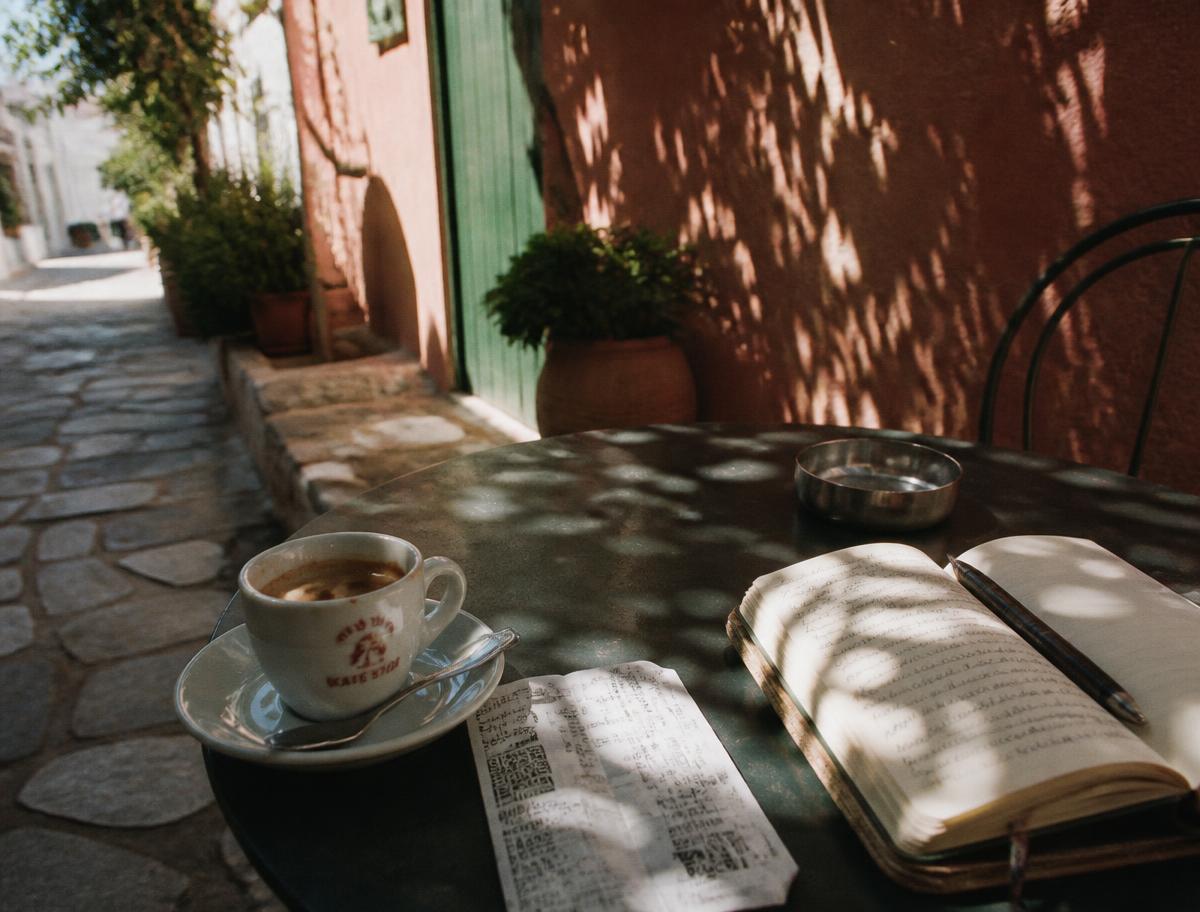 An espresso, a ferry ticket and an open notebook on a café table in a Mediterranean alley